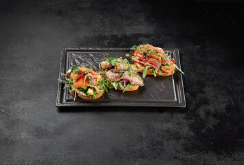 Wall Mural - Assorted bruschetta in black concrete background. Antipasti set: tuna, salmon and roastbeef bruschetta on stone plate. Fish bruschetta and meat bruschetta in minimal style.