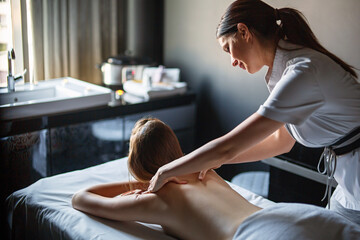 Wall Mural - Happy professional female masseur massaging back of young relaxed woman client on massage table