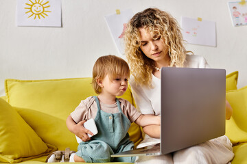 Wall Mural - A curly-haired mother and her toddler daughter sit on a couch, engrossed in a laptop screen.