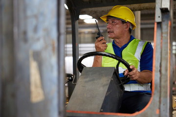 senior worker using walkie talkie and holding steering wheel on forklift truck in the factory