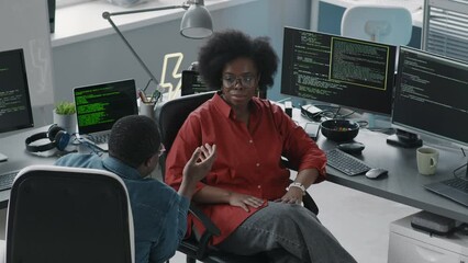 Wall Mural - medium shot of black couple of office colleagues sitting on chairs in front of computers with progra
