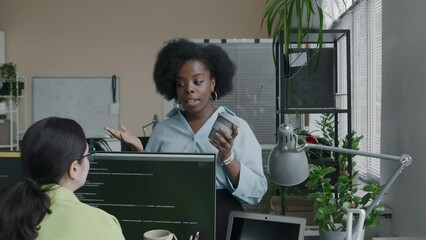 Wall Mural - medium shot of two young ethnically diverse female coworkers chatting during coffee break in office 