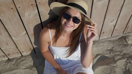 Wall Mural - Beautiful woman in sunglasses and hat enjoying time on   beach, above view. Camera moving right