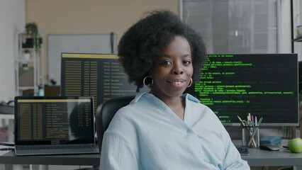 Wall Mural - medium portrait of young african american woman sitting in front of two computer monitors and two la