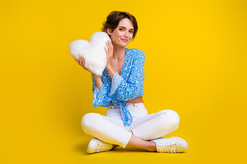 Poster - Full length photo of adorable pretty girl dressed print blouse sit holding fluffy heart shape pillow isolated on yellow color background