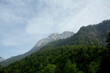 © Connect Images - A picturesque view of a mountain peak rising above a lush green forest under a sky streaked with wispy clouds.