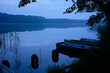 © Image Source - A serene lakeside scene in the early morning featuring rowboats tied to a dock, with a calm reflective water surface and a hint of mist hovering above the lake.