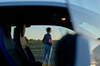 © Image Source - A young woman stands beside a parked car in a field at twilight, gazing into the distance with a contemplative posture.