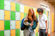 © Connect Images - Two teenagers are standing in a hallway by a row of colorful lockers, engaging with a smartphone together.