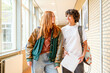 © Connect Images - Two students are walking through a school hallway, smiling and conversing with each other. One is carrying a notebook and the other has a backpack over one shoulder.