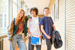 © Connect Images - Three students are smiling and posing in a school hallway, each carrying school supplies.