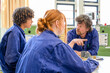 © Connect Images - Three people wearing blue work coveralls are having a discussion in an industrial or workshop environment.