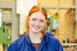 © Connect Images - A smiling young woman with red hair, wearing protective glasses and a blue work shirt, is in an industrial or workshop setting.