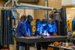© Connect Images - Three individuals are engaged in welding activity in a workshop setting, fully equipped with safety gear including helmets and gloves, as sparks fly from the welding point.