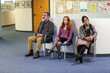 © Connect Images - Three people sitting on chairs in a waiting area of a medical practice