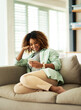 © peopleimages.com - Phone, relax and woman on sofa in home networking on website, mobile app or internet for communication. Smile, rest and female person scroll on social media with cellphone in living room at house.