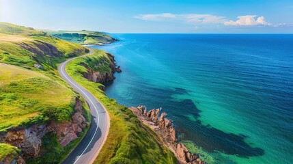 Canvas Print - Overhead view of a winding coastal road with vibrant green cliffs on one side and a deep blue sea on the other, under a clear azure sky.