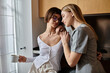© Bliss - A young lesbian couple standing with coffee cup, chatting in a cozy hotel kitchen.