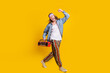 © deagreez - Full body profile portrait of cool young man raise fist walk empty space boombox wear denim shirt isolated on yellow color background