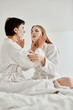 © Bliss - Two women, a beautiful lesbian couple in bath robes, sit on a bed. lesbian couple wear face masks