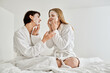 © Bliss - Two women in bath robes sitting on a bed, calmly wearing face masks for a spa-like moment of relaxation.