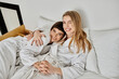 © Bliss - A beautiful lesbian couple in bath robes lying together on a plush hotel bed, sharing a tender moment.