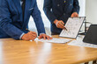 © M+Isolation+Photo - A team meeting of business people and a lawyer in formal suits is taking place at a desk, discussing a contract and various aspects of the law and litigation.