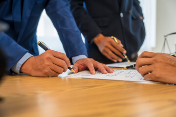 A team meeting of business people and a lawyer in formal suits is taking place at a desk, discussing a contract and various aspects of the law and litigation.