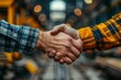 © familymedia - Close-up view of two workers shaking hands in a factory environment, symbolizing teamwork