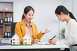 © NanSan - Asian businesswoman discusses home purchase contracts with clients at her desk, focusing on loans, mortgages, and other financial aspects of real estate transactions.