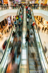 View of a large shopping center with an escalator carrying a crowd of people in motion blurred view