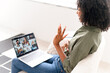 © Vadim Pastuh - An African-American woman warmly greets a group of diverse colleagues in a virtual meeting, exuding friendliness and professionalism from her stylish living room