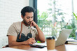 © Ekkasit A Siam - Multiethnic male business employee, brown shirt, overalls, cafe owner Sitting working  tablet writing down raw materials, don't think about it.disposable paper coffee cup front  him. Small family cafe