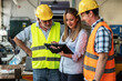 © BalanceFormCreative - A supervisor stands confidently with workers on the factory line, using a tablet to check the numbers and quality of production.