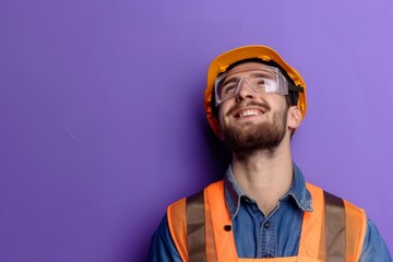 A male construction worker in a hard hat and goggles against a purple wall.