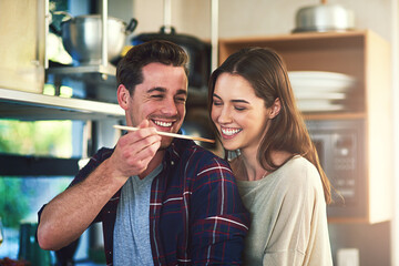 Canvas Print - Man, woman and together with spoon for taste test in kitchen, cooking with check on soup for approval. Couple, happiness or nutrition in home for wellness, healthy food for natural vitamins in winter