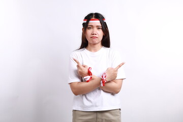 Confused Asian young woman with red white ribbon for celebrating Indonesia independence day standing while pointing right and left side