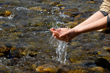 Women's hands, water is pouring near a river, sea, ocean. People in nature. Ecology. A woman touches the water with her hands.