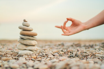 A hand is shown in front of a stack of rocks. The hand is in a yoga pose, and the rocks are arranged in a pyramid shape. Concept of balance and harmony, as the hand