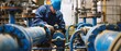 © Sittipol  - An industrial worker in a hard hat and blue coveralls inspects a large blue pipe.