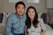 © AIPhoto - Happy couple sitting on bed, smiling and holding hands in cozy room interior with soft lighting.