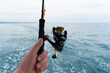 © Aleksei - Hands of a fisherman with a spinning rod with the line with a line on a motor boat in the sea.  Fishing rod and hands of fisherman over ocean water surface.