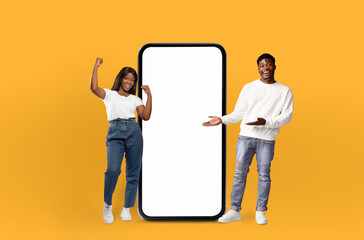 Wall Mural - African American man and woman are standing side by side, looking at a phone with a blank screen. They appear to be engaged in a conversation or activity involving the device.