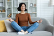 © Tetiana - Smiling young woman relaxing on sofa at home, relaxing with yoga, sitting in lotus position with closed eyes and meditating peacefully