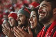 © ELIJA - A group of people wearing red hats and scarves, cheering and clapping as enthusiastic football fans in the stands