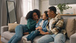 © Yuliia - Excited happy smiling African American ethnic family woman little boy strong man bringing new sofa couch furniture apartment then mother father son sitting hugging relaxing enjoying rest indoors home