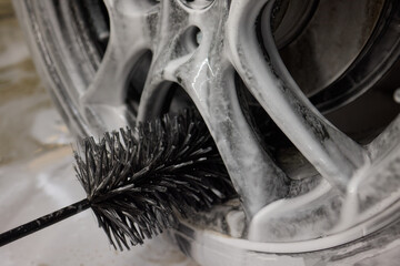 Cleaning car wheel thoroughly with brush and soap for maintenance and shiny result