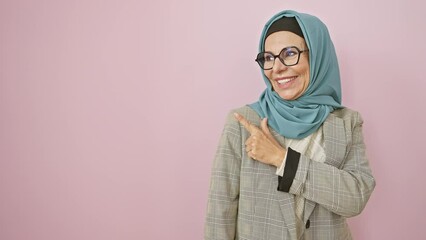 Canvas Print - Cheerful middle age hispanic woman in hijab, smile beaming, happily points upwards with finger! natural expression against isolated pink background, joyfully directing your attention sideways.