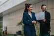 © qunica.com - Two smiling businesswomen discussing documents in an urban outdoor setting, expressing success and teamwork.