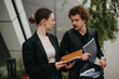© qunica.com - Two business professionals engaged in an outdoor conversation, exchanging notebooks in a modern city setting, conveying teamwork and communication.